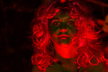 The face of the woman of the forest witch is a close-up in the gleam of red light. Light falls on the face.