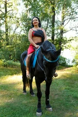 Foto op Canvas Beautiful brunette in a red suit in a saddle on a horse in the forest. Overall plan. © finist_4