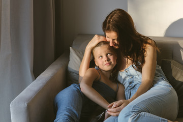 Smiling mother and daughter sitting on sofa at home
