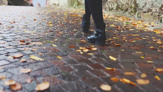 woman walking on wet pavement in old town in autumn Europe, close up of feet, fall season