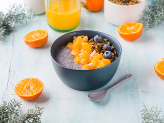 Chia pudding with tangerines and matcha tea granola in a bowl on pastel turquoise wooden background. Plant based breakfast