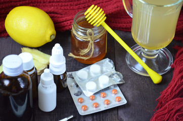 healthcare, traditional medicine and flu concept - tea cup with lemon, ginger, honey and pills on wooden table. tablets, pills, cough syrups, nasal drops and non-traditional alternative medicine.