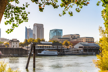 Sacramento's skyline and waterfront framed by tree branches, as seen from the banks of Sacramento river of a sunny morning; California