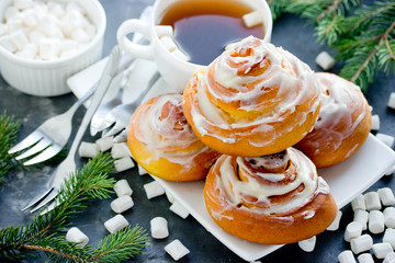 Obraz na płótnie Canvas Pumpkin cinnamon rolls with cheese frosting on dining table with christmas tree branches and marshmallow