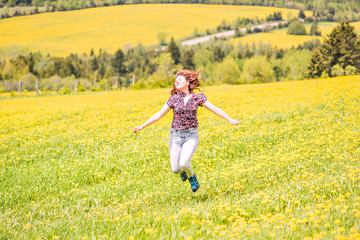 Fototapeta premium Back of young woman running, jumping in air and smiling on countryside yellow dandelion flower fields in summer grass in Ile D'Orleans, Quebec, Canada back