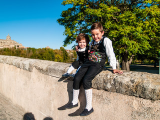 Two children brothers embraced on the Roman bridge of Salamanca, dressed in traditional clothes
