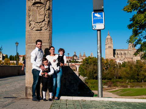 One family traveling with two children brothers embraced on the Roman bridge of Salamanca, dressed in traditional clothes and Salamanca cathedral