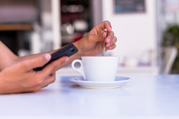 close up view of woman hands holding a cup of coffee and mobile phone in a terrace. Morning, daytime and technology