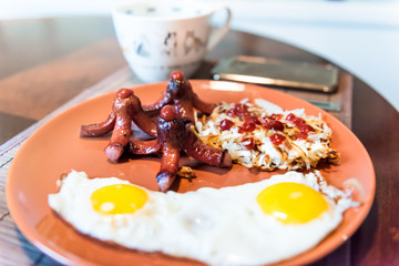 Large breakfast brunch plate closeup with fried eggs, hash browns shredded potatoes, ketchup, sausage tako octopus, coffee cup, smartphone phone