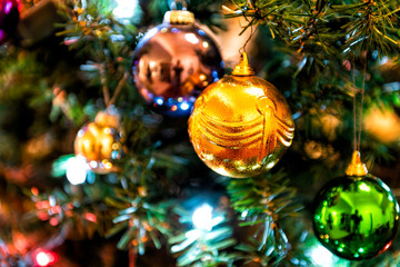 Obraz na płótnie Canvas Closeup of hanging illuminated orange, green, blue, colorful, multicolored, multi-colored Christmas ornament on pine tree with lights