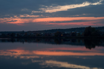 Village on the lake at sunset. Evening landscape with a reflection of the sky in the water.