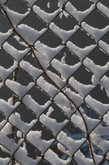 Detail of an overgrown chain link fence with snow covered with fresh snow piled in the links.