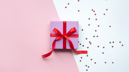 Holiday gift with bow on pink and white background, top view, copy space.