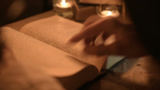 Big Close-up girl magician in a dark room with candlelight looking for a spell in a book. Low key live camera. Mystic. Small DOF