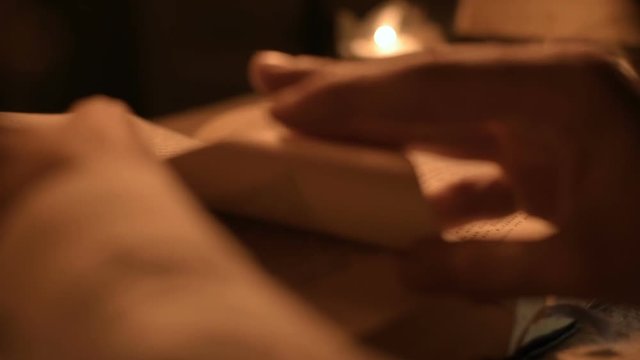 Big Close-up girl magician in a dark room with candlelight looking for a spell in a book. Low key live camera. Mystic. Small DOF