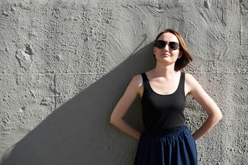 young girl posing against a concrete wall, dressed in black, hard light and shadows