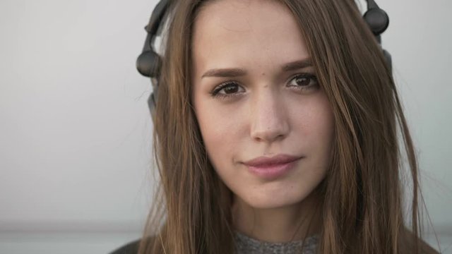 Extreme close up slow motion young stylish long hair brunette woman big dj headphones enjoying music dancing, smiling on the wind metal panels city wall