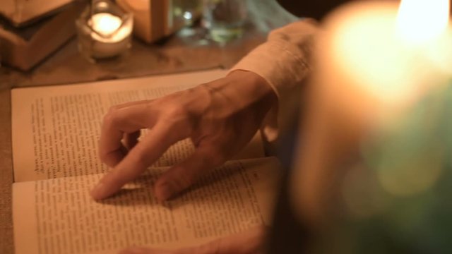 Big Close-up girl magician in a dark room with candlelight looking for a spell in a book. Low key live camera. Mystic. Small DOF