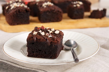 Chocolate brownie with nuts on white plate with spoon