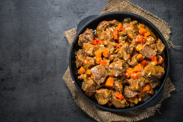 Beef stew with vegetables in iron pan on black.