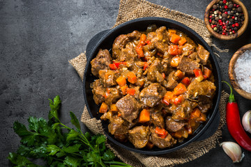 Beef stew with vegetables in iron pan on black.