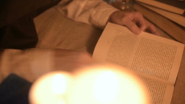 Big Close-up girl magician in a dark room with candlelight looking for a spell in a book. Low key live camera. Mystic. Small DOF
