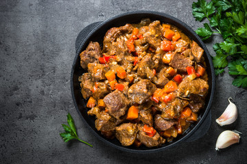 Beef stew with vegetables in iron pan on black.