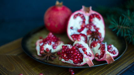 Fototapeta na wymiar broken pomegranate lies on a plate, the branches of spruce lie in the background (horizontally)