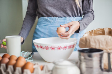 A woman prepares the dough for the pie, breaks an egg into a cup. On the table are ingredients for making dough.selective focus.
