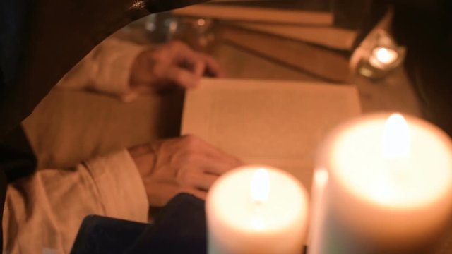 Big Close-up girl magician in a dark room with candlelight looking for a spell in a book. Low key live camera. Mystic. Small DOF