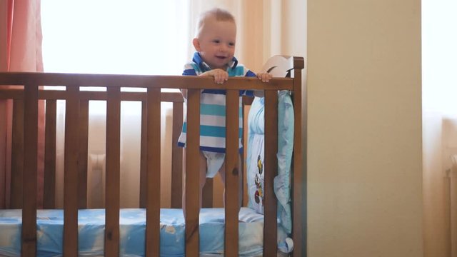 Little funny boy standing in baby bed and laughing. Smiling adorable child on feet in playpen. Happy childhood concept.