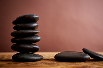 stack of black spa stones for massage on a brown background and an old wooden table
