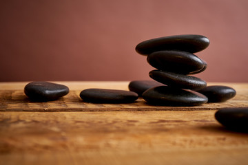 stack of black spa stones for massage on a brown background and an old wooden table