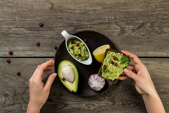Closeup top view of woman hands eating sandwich with guacamole sauce