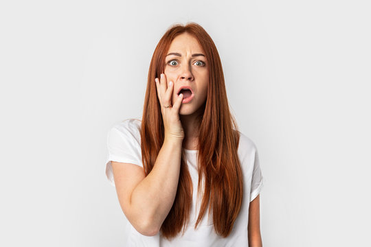 Closeup photo of young emotional European female isolated on grey background. Red-haired girl in a white T-shirt. Expression of absolute deep surprise with great news.