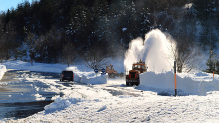 Dangerous and slippery snowy mountain road with snowdrifts and snow blower. Winter service vehicle