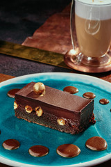 Brownie cake with whole nuts and cappuccino. Chocolate cake with hazelnuts on a blue plate on a background of copper plates. Close up