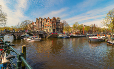 Spring sunny Amsterdam. The bright clear blue sky with white clouds. Boat trip on the canals of Amsterdam. The bridge over the water. Travel to Europe