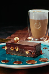 Brownie cake with whole nuts and cappuccino. Chocolate cake with hazelnuts on a blue plate on a background of copper plates. Close up