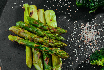 portion of grilled asparagus on a round black plate on a copper background. close up.