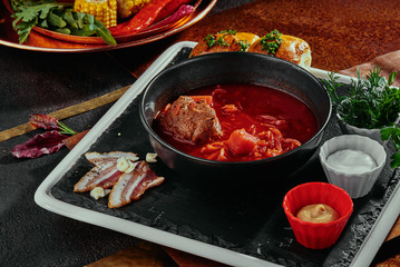 Homemade Russian, Ukrainian and Polish national soup - red borsch made of beetrot, vegetables and meat with sour cream in a black plate on a copper background. close up