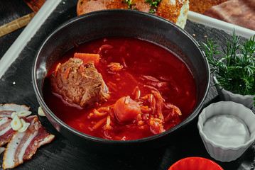 Homemade Russian, Ukrainian and Polish national soup - red borsch made of beetrot, vegetables and meat with sour cream in a black plate on a copper background. close up