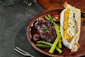 Fermented steak. juicy steak with asparagus and corn grilled served on a round brown plate on a copper sheet background. close up. Photo series