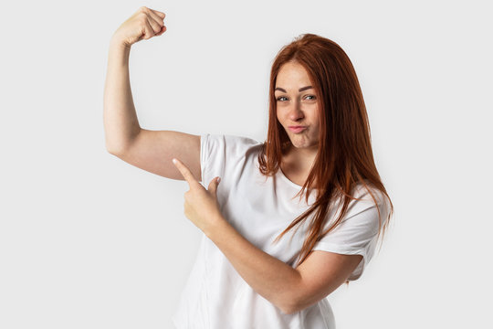 Portrait of young beautiful redhead European girl isolated on white background. Showing biceps muscle having lifted arm with clenched fist