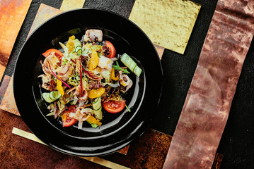 salad with ham, orange slices, tomato, cucumber and lettuce leaves in a black plate on a copper background. close up