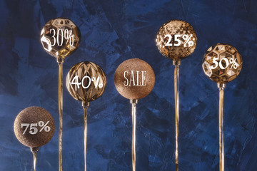 Golden Christmas balls on blue background. The balls are turned upside down with the words Sales and numbers with percentages on them. Unusual concept.