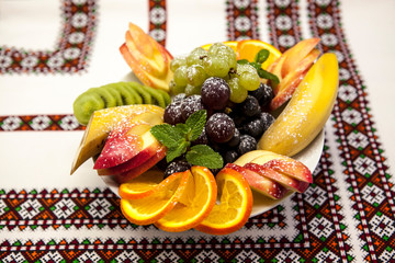 Plate with fresh fruits for the holidays: banana, grapes, orange, apple, kiwi, mint