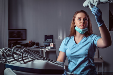 Female dentist adjusting lighting equipment over a chair in the dental clinic.