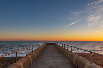 Fototapeta premium Looking down a jetty out to sea, with a sunset sky behind