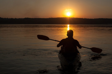 A man paddling on kayak silhouette in sunset, view from the back